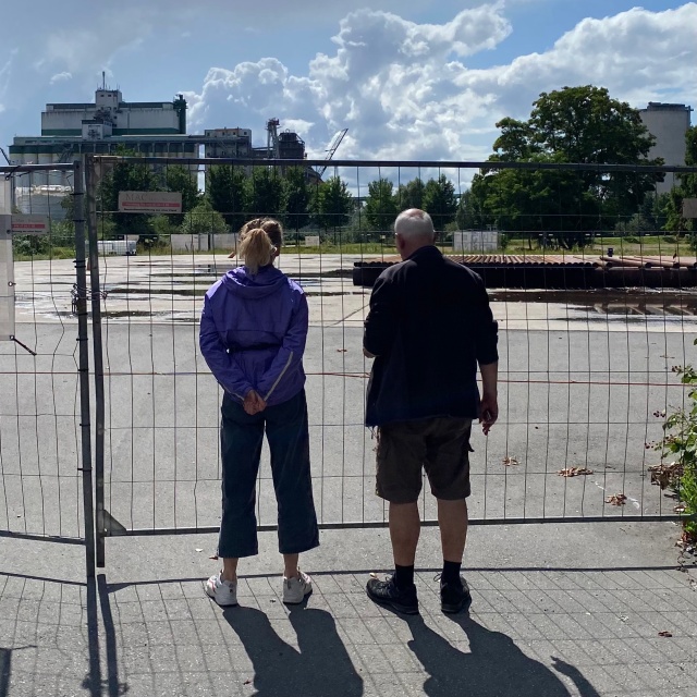 Zwei Menschen stehen mit dem Rücken zur Kamera vor einem Absperrzaun in Wilhelmsburg